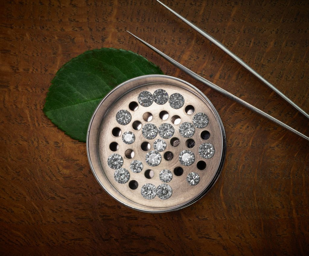 Ethical lab-grown diamonds photograph showing small round diamonds in a diamond sorting sieve on wood background with gemstone tweezers.