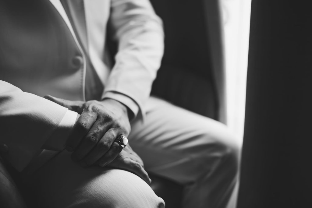 A man in a suit with a signet ring on his little finger sits by the window, close-up, black and white